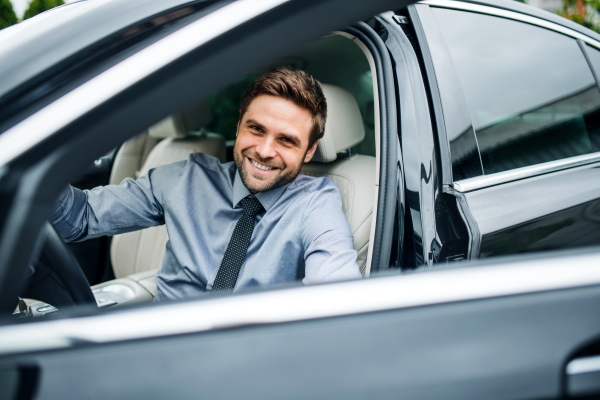 Happy young man with blue shirt and tie getting out of car in town.