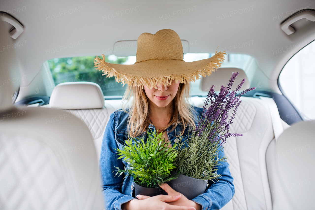 Front vieww of young woman with hat and plants sitting in car, having fun.