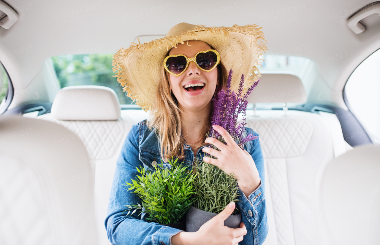 A young woman with hat and sunglasses sitting in car, holding plants.