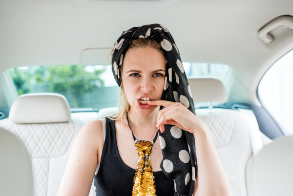 Young crazy woman sitting on back seat in car, going on a party and having fun.