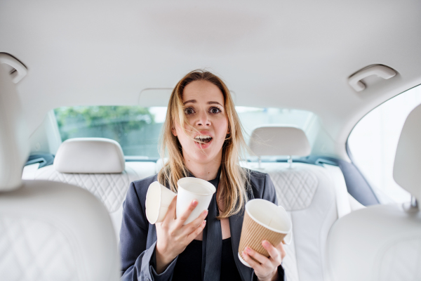 Young frustrated woman with empty paper glasses sitting in car, longing for coffee.