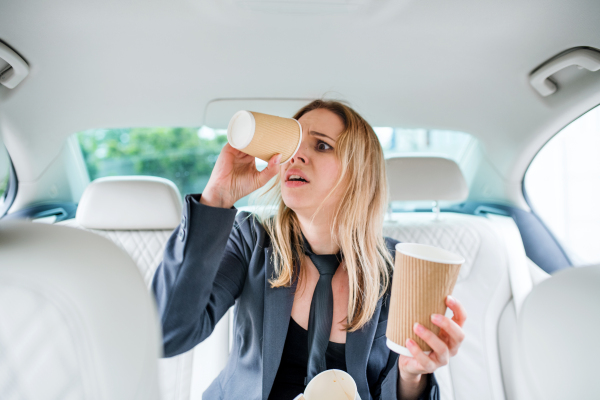 Young frustrated woman with empty paper glasses sitting in car, longing for coffee.