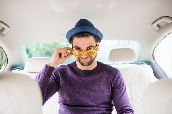 A cheerful man with party accessories sitting in car, having fun