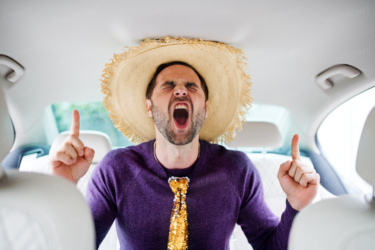 A cheerful man with party accessories sitting in car, having fun