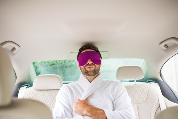 A cheerful man with dressing gown and eye mas sitting in car, resting.