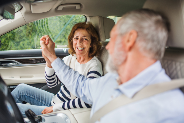 A happy senior couple with smartphone sitting in car, talking.