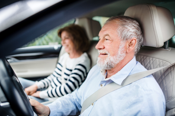 A happy senior couple with smartphone sitting in car, driving.