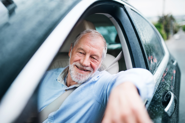 A happy senior man sitting in car in driver seat.