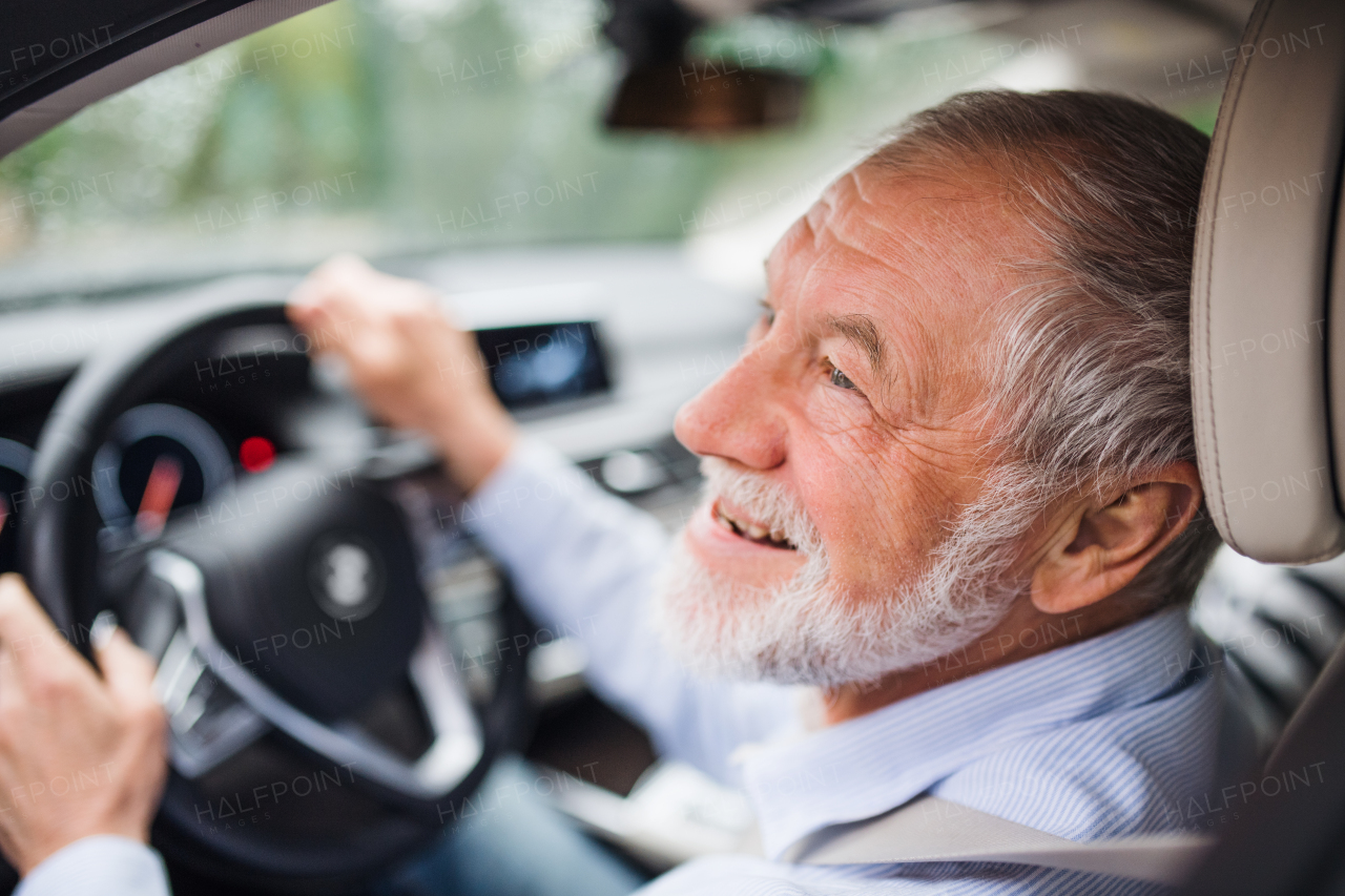 A close-up of happy senior man sitting in car in driver seat, driving.