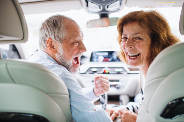 A rear view of happy senior couple sitting in car, looking back.