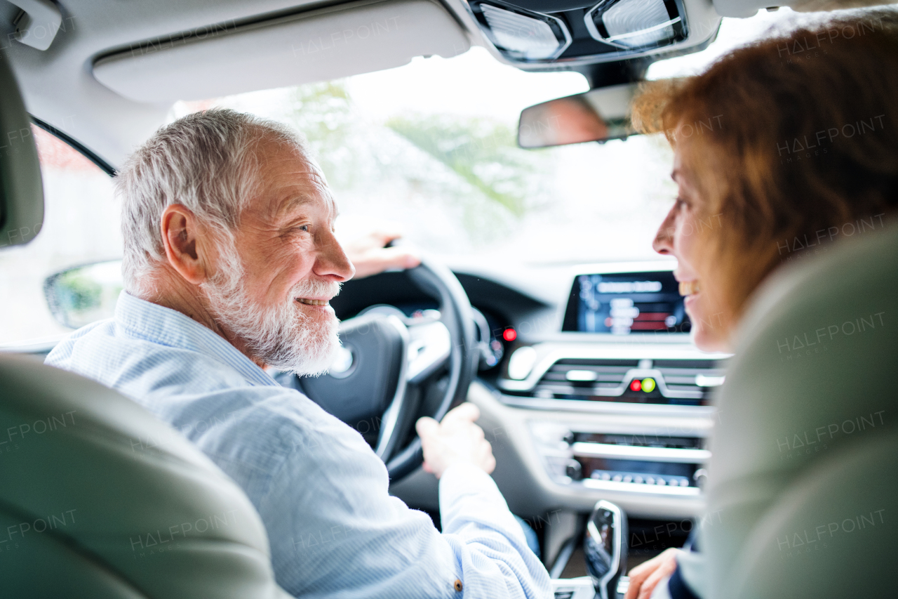 A rear view of happy senior couple sitting in car, talking.