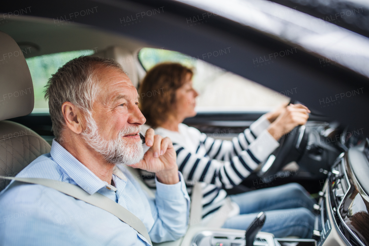 A happy senior couple with smartphone sitting in car, talking.