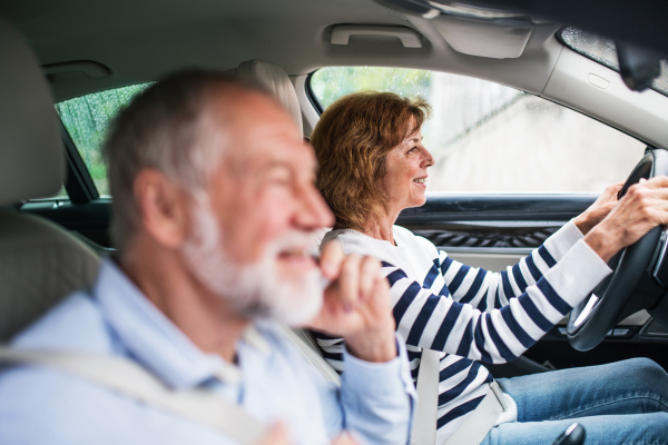 A happy senior couple with smartphone sitting in car, going on trip.