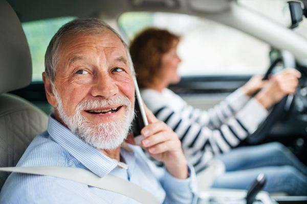 A happy senior couple with smartphone sitting in car, going on trip.