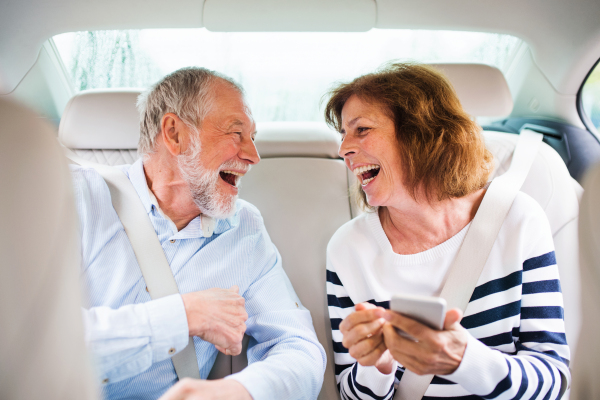 A cheerful senior couple sitting on back seats in car, laughing.