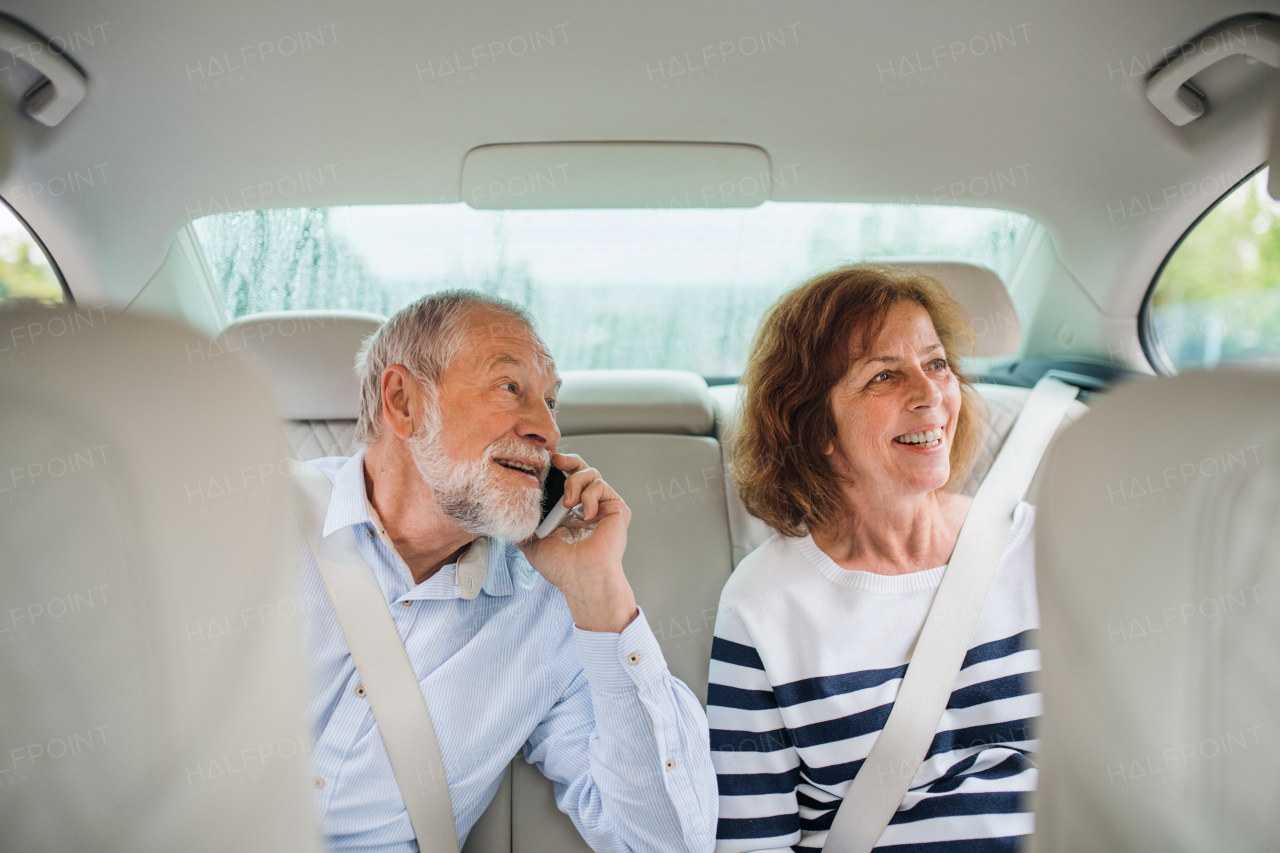 A happy senior couple with smartphone sitting in car, talking.