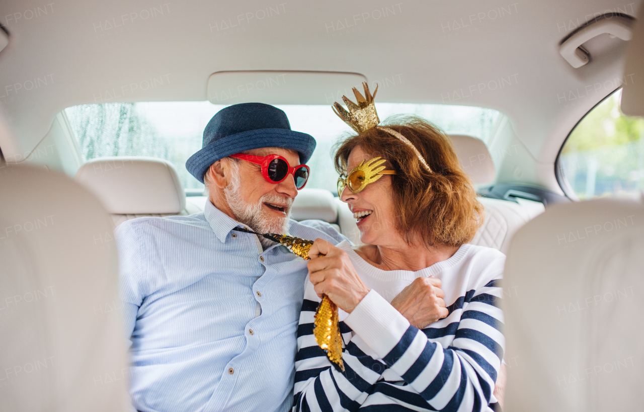 A cheerful senior couple with party accessories sitting in car, having fun.