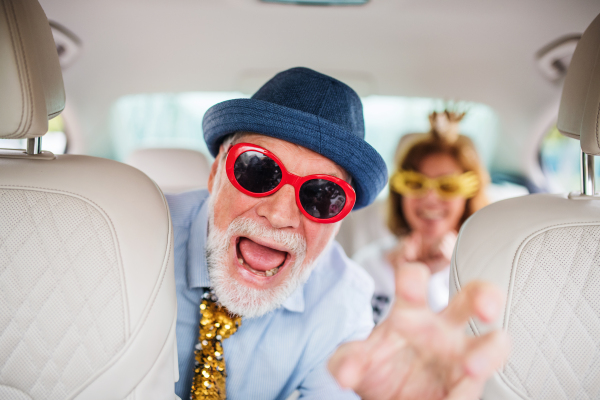 A cheerful senior couple with party accessories sitting in car, having fun.