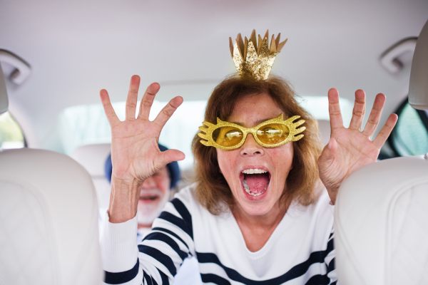 A cheerful senior couple with party accessories sitting in car, having fun.