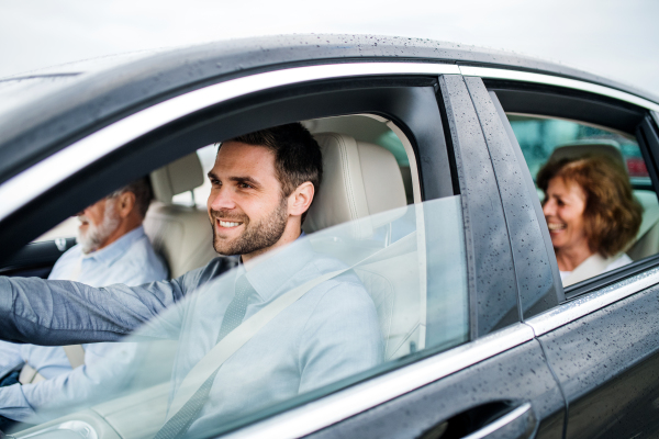 A mature son with senior parents sitting in car, driving and talking.