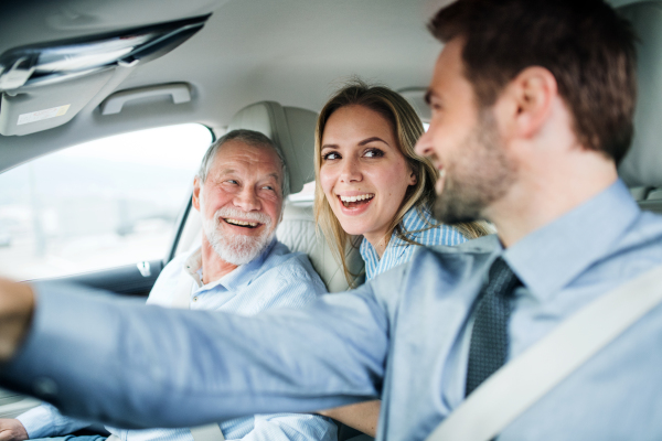 A young couple with senior father sitting in car, driving and talking.