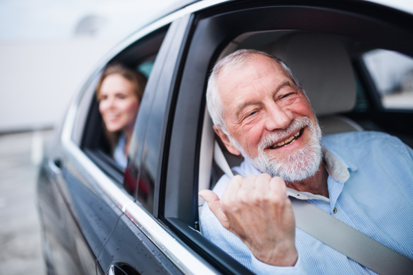 A senior man and young woman sitting in car, looking out of window.