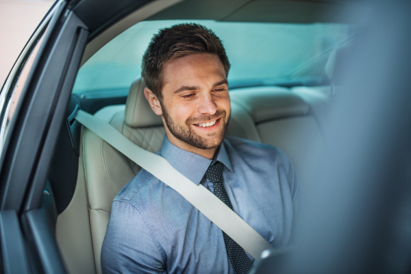 A businessman with tablet sitting on back seats in car, working.