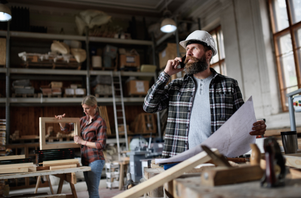 Low angle view of a mature male carpenter looking at blueprints plans in carpentery workshop. Small business concept.