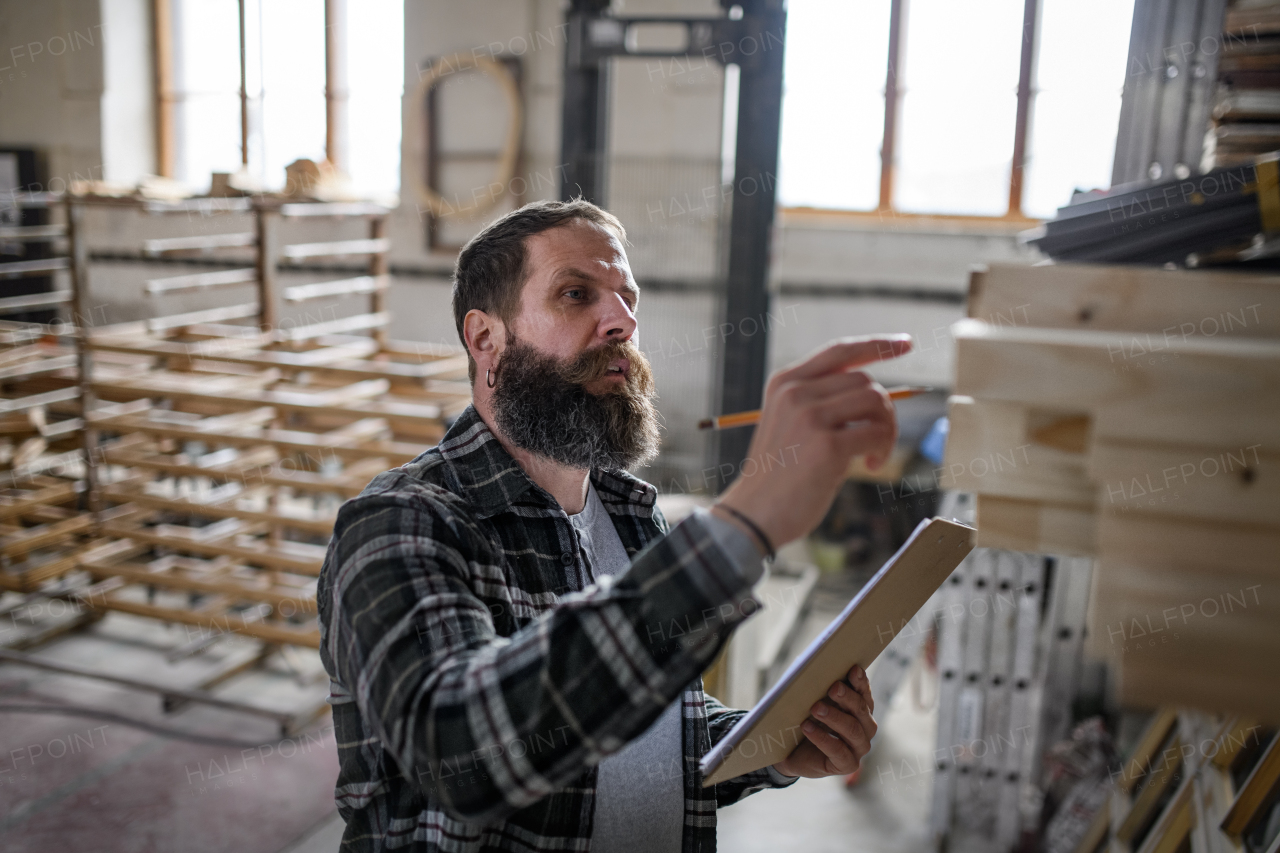 A mature male carpenter checking inventory indoors in carpentery workshop. Small business concept.