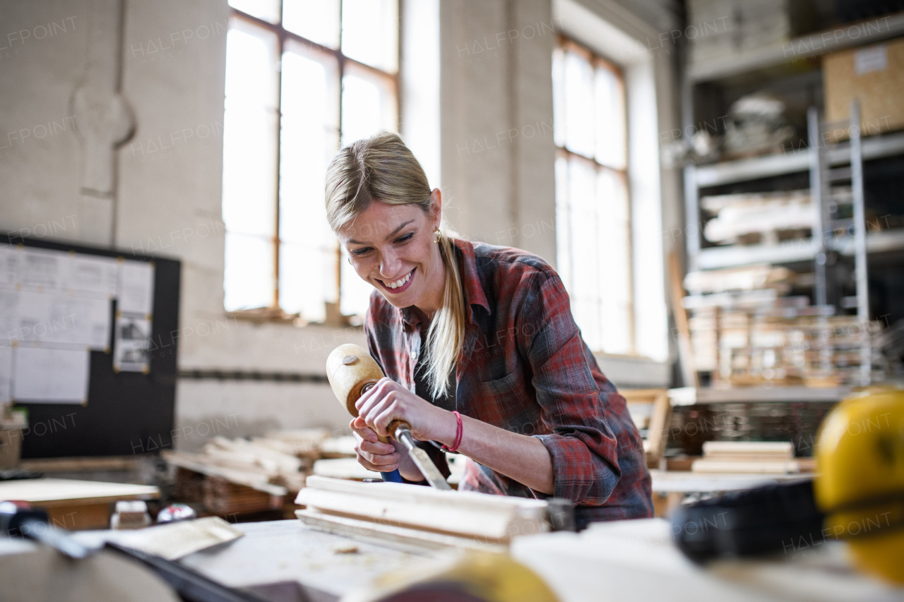 A happy female carpenter working on her product indoors in carpentry workshop.