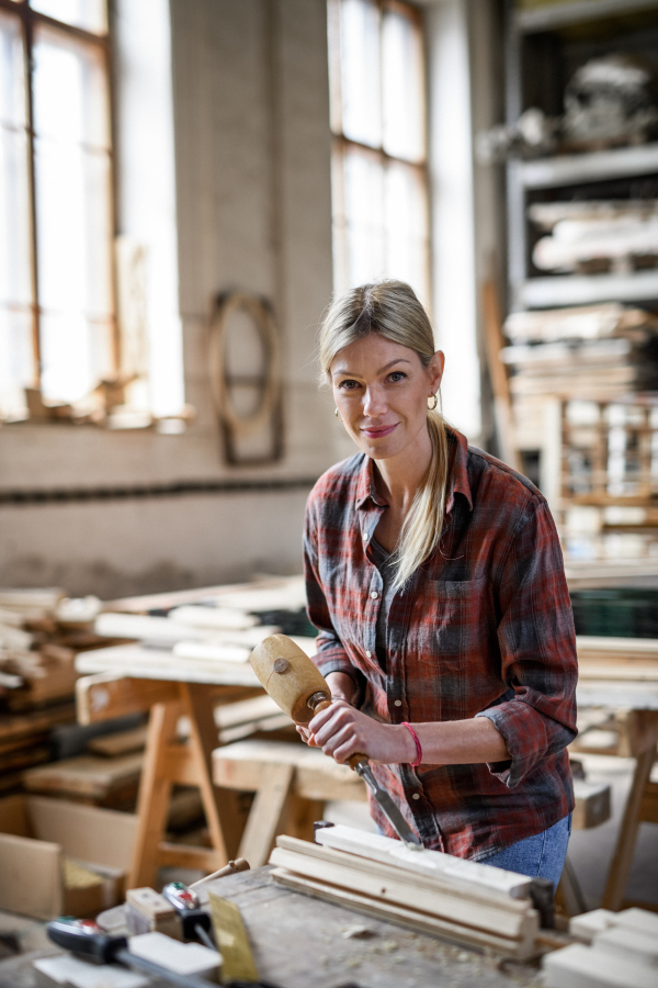 A female carpenter with goggles working on her product, looking at camera. Small business concept.