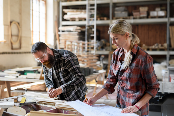 Two carpenters man and woman looking at blueprints indoors in a carpentery workshop.