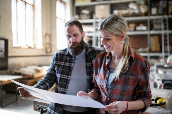 Two carpenters man and woman looking at blueprints indoors in a carpentery workshop.