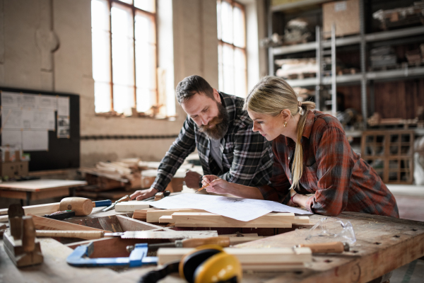 Two carpenters man and woman looking at blueprints indoors in a carpentery workshop.