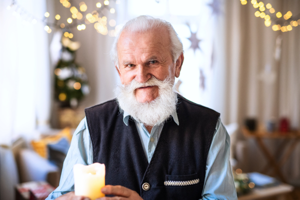 Front view of happy senior man with candle indoors at home at Christmas, looking at camera.