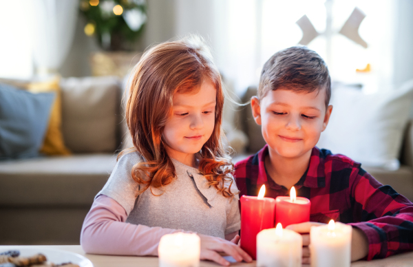 Portrait of small girl and boy indoors at home at Christmas, holding candles.