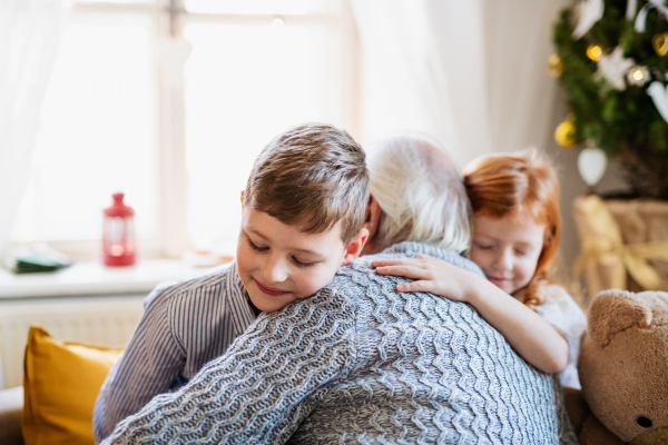 Small children with unrecognizable senior grandfather indoors at home at Christmas, hugging.