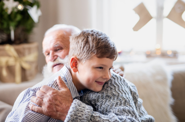 Portait of small boy with senior grandfather indoors at home at Christmas, hugging.