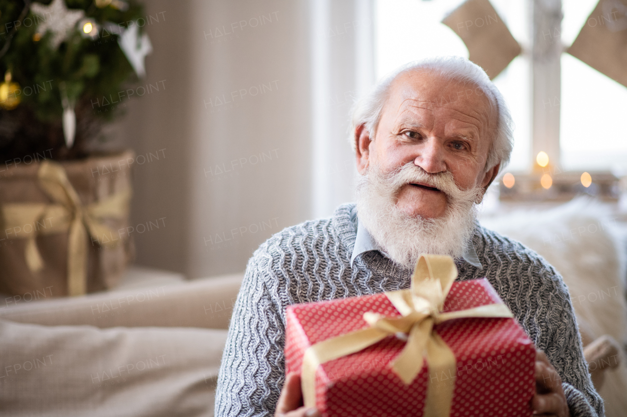 Front view of happy senior man with present box indoors at home at Christmas, looking at camera.