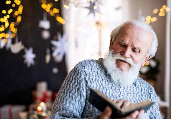 Front view portrait of happy senior man indoors at home at Christmas, reading book.