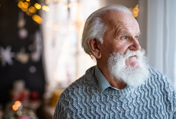 Front view of sad and lonely senior man indoors at home at Christmas. Copy space.