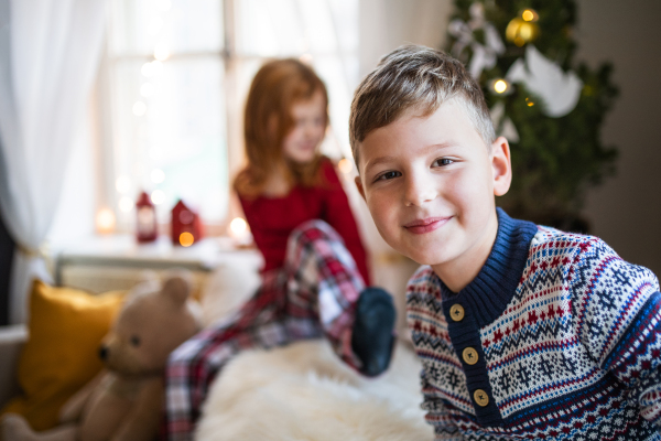 Happy small girl and boy in pajamas indoors at home at Christmas, playing.