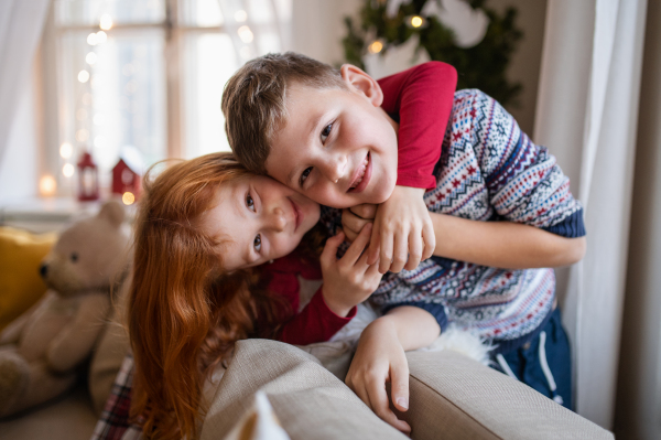 Portrait of small girl and boy indoors at home at Christmas, looking at camera.