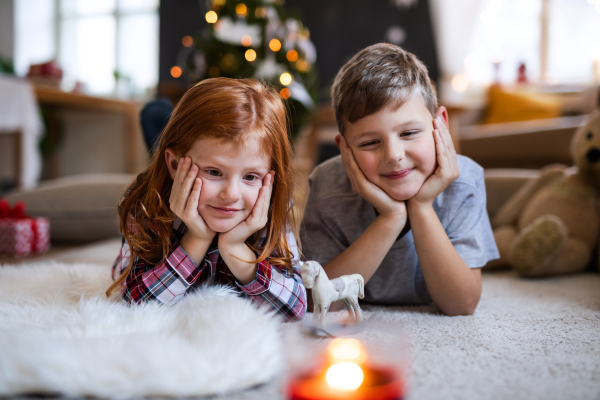 Front view of small girl and boy indoors at home at Christmas, lying on the floor.