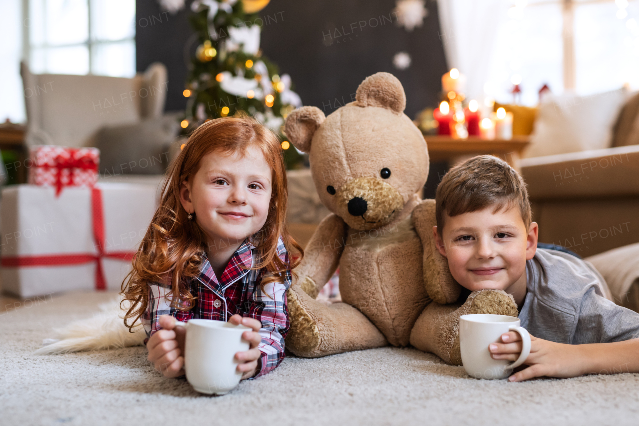 Small girl and boy in pajamas on floor indoors at home at Christmas, looking at camera.