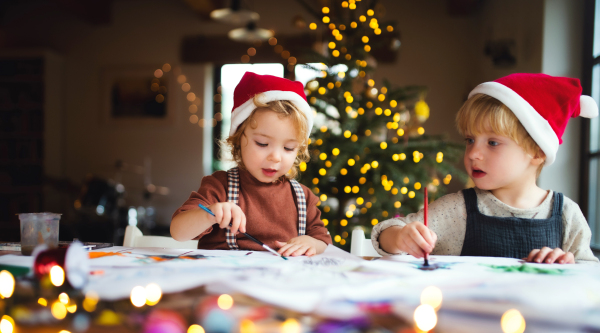 Portrait of happy small girl and boy indoors at home at Christmas, painting pictures.