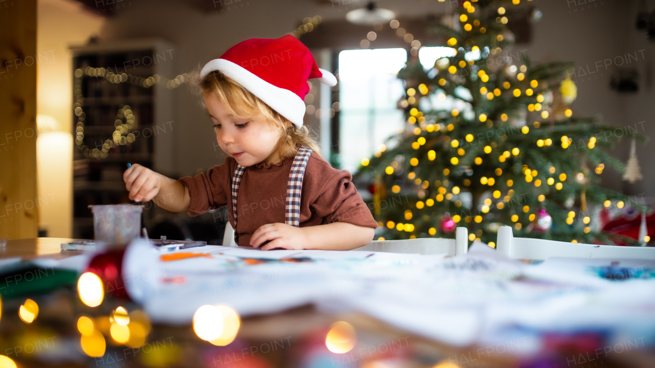 Portrait of happy small girl indoors at home at Christmas, painting pictures.