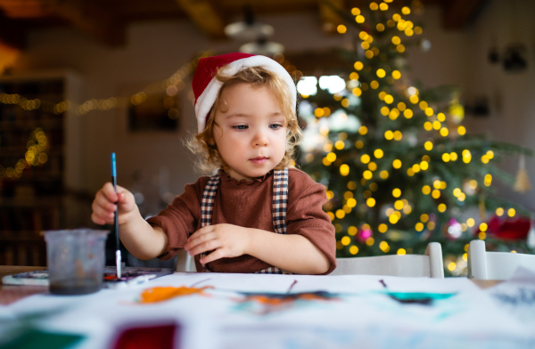 Portrait of happy small girl indoors at home at Christmas, painting pictures.