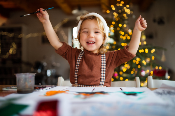 Portrait of happy small girl indoors at home at Christmas, painting pictures.