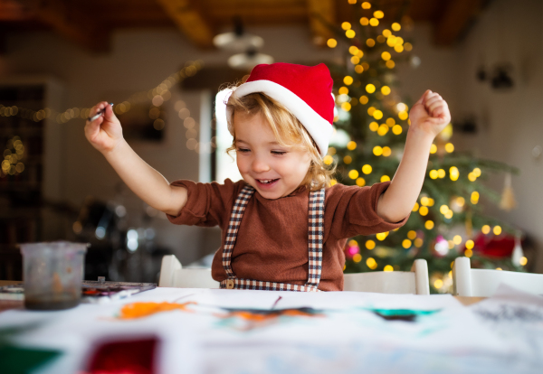 Portrait of happy small girl indoors at home at Christmas, painting pictures.